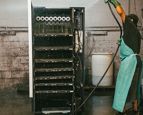 a man washes a vending machine by spraying it with water from a hose